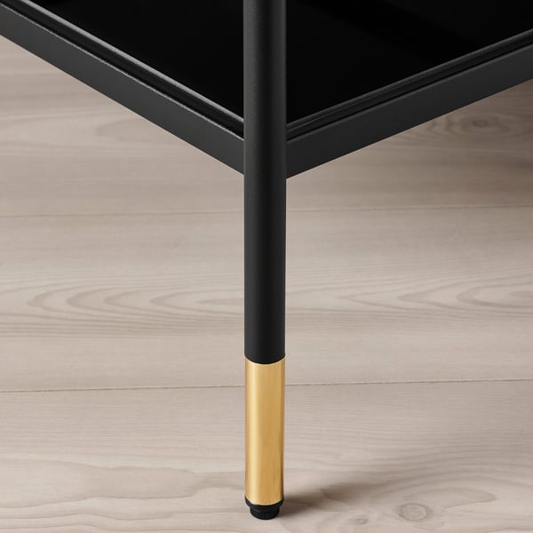 Modern black and gold table leg on wooden floor.