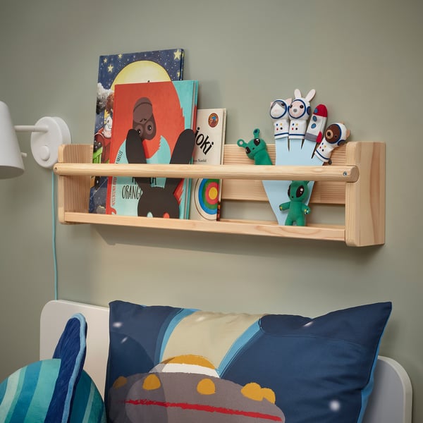 Wooden shelf with kids books & toys above blue bed.