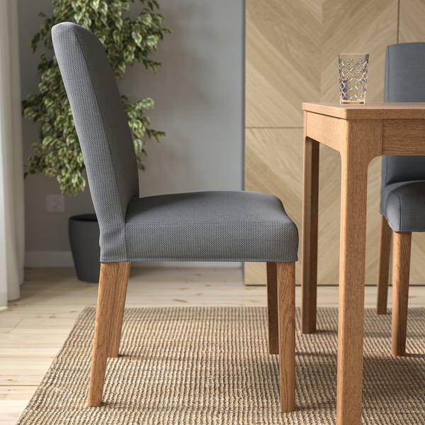 A grey upholstered chair with wooden legs sits near a wooden table on a woven rug. The chairs design offers comfort and style, easy to clean.