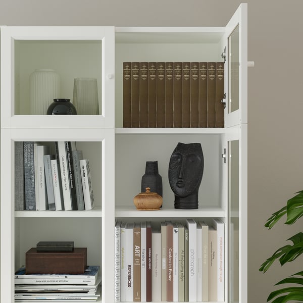 White bookcase with adjustable shelves, displaying books and decorative items. One shelf has glass doors.