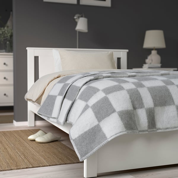 White BORSTTÅG bedspread with grey check on large bed against dark wall.