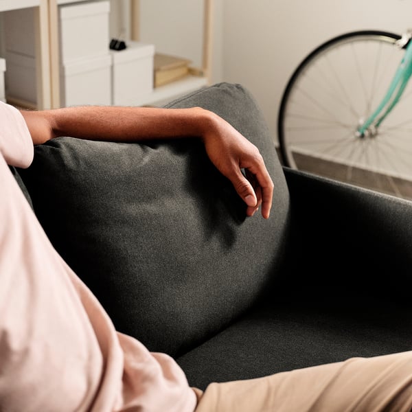 A person sitting on a grey GLOSTAD sofa, arm on the padded armrest, showing comfort and easy assembly.