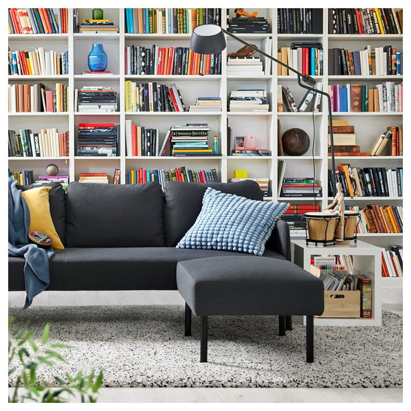 Cosy living room with GLOSTAD grey sofa and filled bookshelf, adorned with colourful pillows.