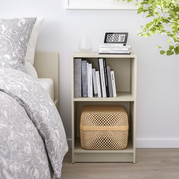 Beige GURSKEN bedside table beside bed with books, clock, basket.