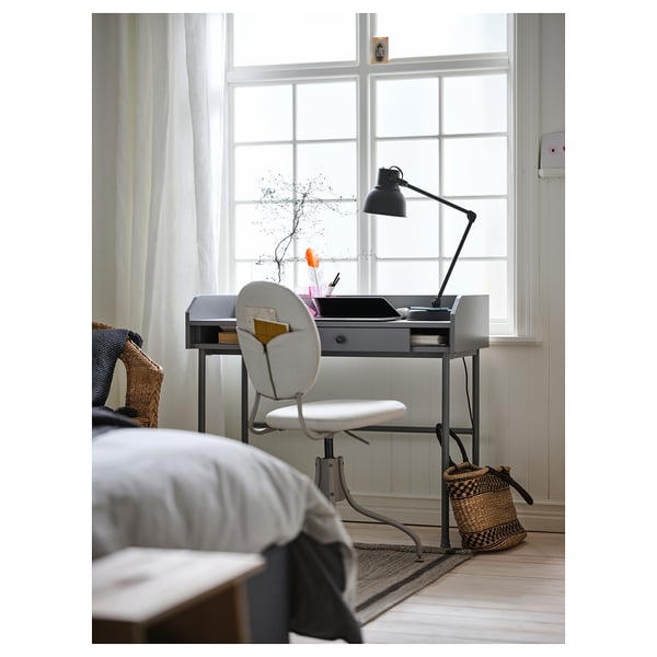 Home office setup with HAUGA desk, white chair, lamp, and basket; minimalist, well-lit.