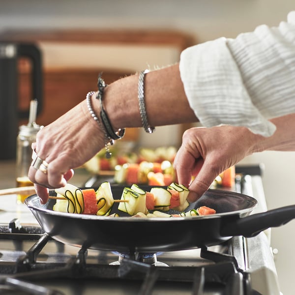 Person cooking colourful veggies in a non-stick frying pan on a stove.