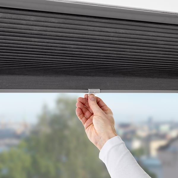 Person opens darkening window blind, revealing city view.