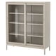 An IDÅSEN cabinet in beige. It has glass sliding doors and four interior shelves. The modern design is sturdy with a metal frame and tempered glass.