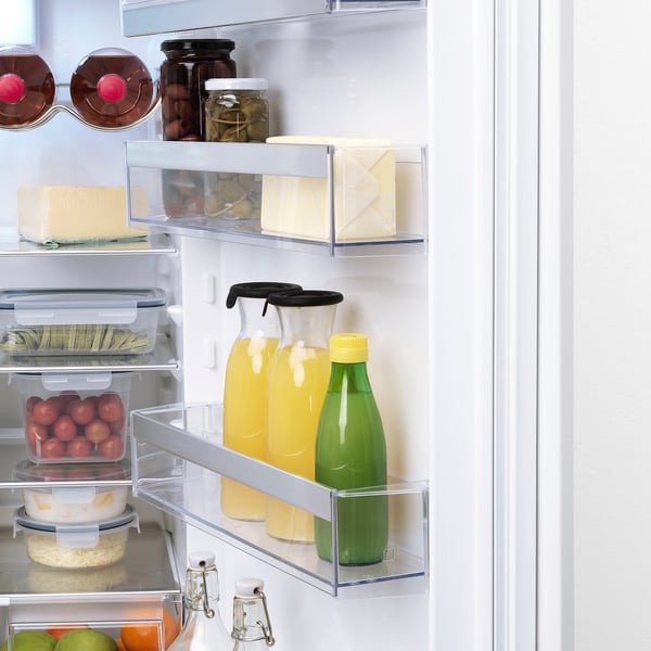 Fridge door open, showing fruits, juices, and cheese. Clear storage boxes and adjustable shelves.