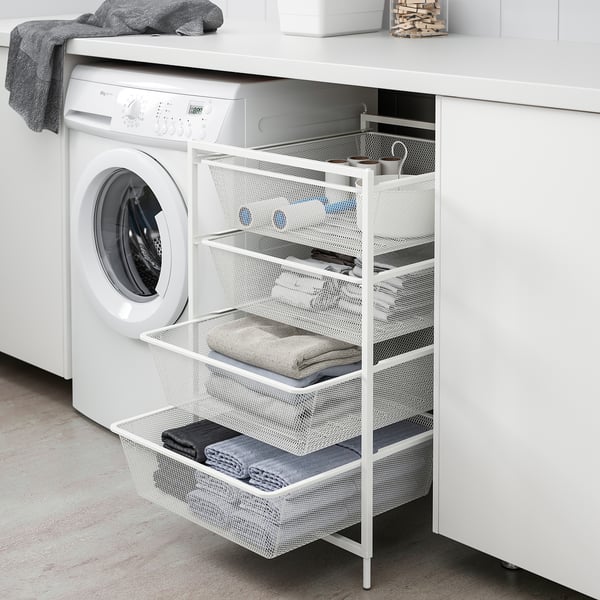 A JONAXEL white mesh storage unit next to a washing machine, holding towels and laundry supplies, ideal for small spaces.