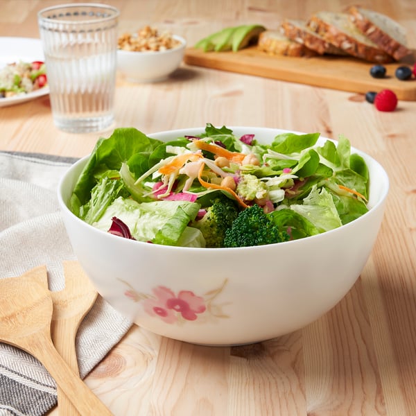 Floral salad bowl on wooden table with plates and cutlery, durable & dishwasher-safe.