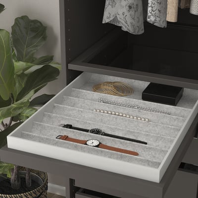 Open jewellery tray with watches, pearls, & bracelets in sections, beside a plant.