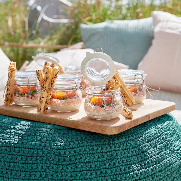 Small glass jars on wooden tray, sealed, holding snacks and dips. Ideal for picnic or outdoor dining, showcasing KORKENs airtight seal.