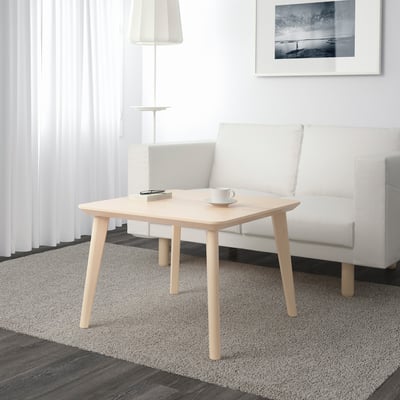 Small, light wooden coffee table holds a cup and remote, next to a white sofa.