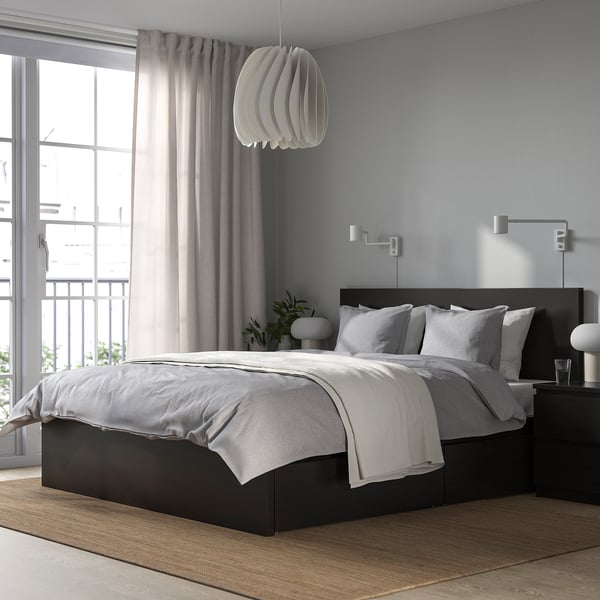 Modern bedroom with black bed, grey bedding, hanging light, large window, two nightstands, wall lamps, plants.