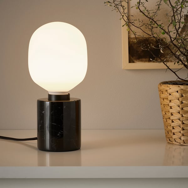 A modern table lamp with a black marble base and a round white globe light bulb sitting on a shelf. The warm light adds cosy ambiance to the room.