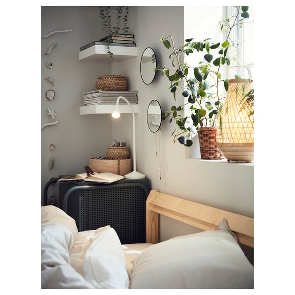 Cosy bedroom with white bedding, wooden headboard, books, plants, mirrors, and adjustable NÄVLINGE lamp.