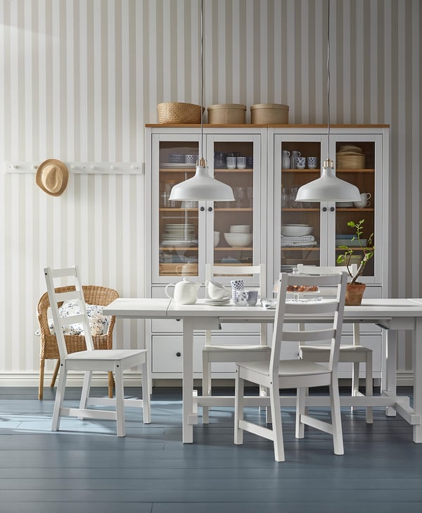 Modern dining area with a white NORDVIKEN table and chairs, grey striped walls, and glass cabinet with dishes.