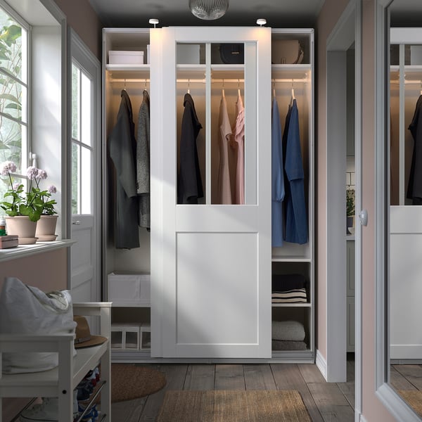 Modern white PAX wardrobe with glass doors, showing clothes.