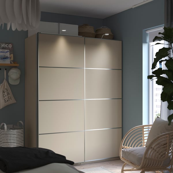 Modern bedroom with large beige PAX wardrobe, bed, wicker chair, and plants.