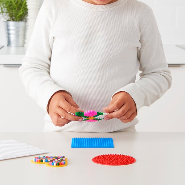 A child holding colourful plastic beads, creating a design on a blue bead board.
