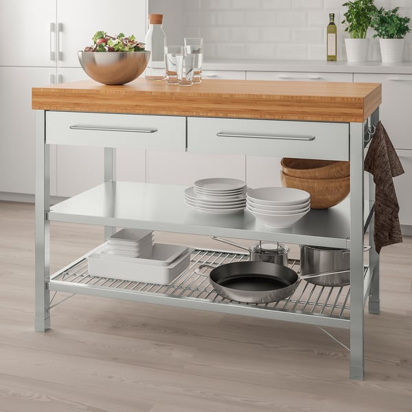 IKEA RIMFORSA grey kitchen island with bamboo top, glass shelves, and stainless steel accents, holding plates, bowls, and a frying pan.