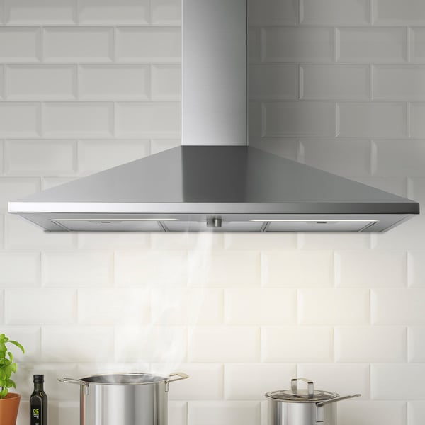 Stainless steel kitchen hood with led lights mounted on white tiled wall, flanked by pots and a plant.