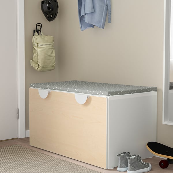 Wooden storage box for kids toys with cushioned lid, near skateboard, trainers, and wall hangings.