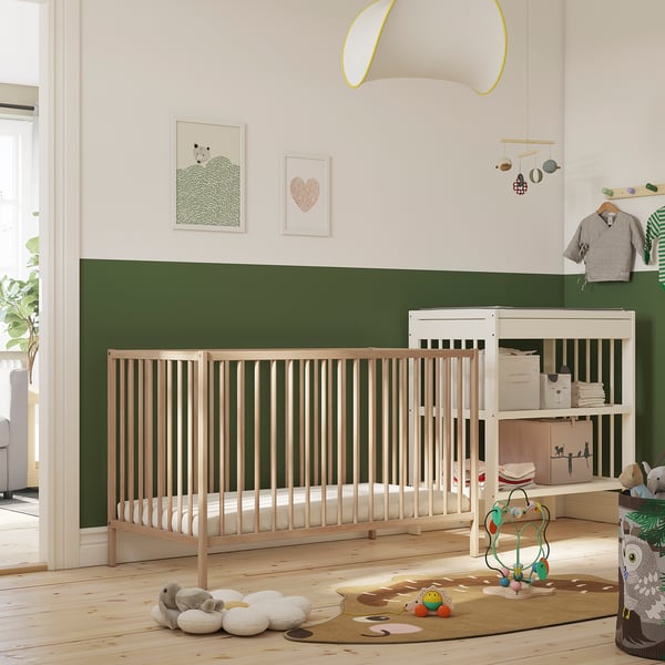 Bright nursery with SNIGLAR crib, changing table, toys, and art. Crib centred, larger than toys, smaller than frames.