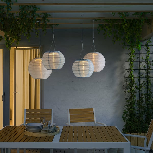 Outdoor dining table with SOLVINDEN solar lanterns. Wooden chairs, plates, utensils. Soft evening glow.