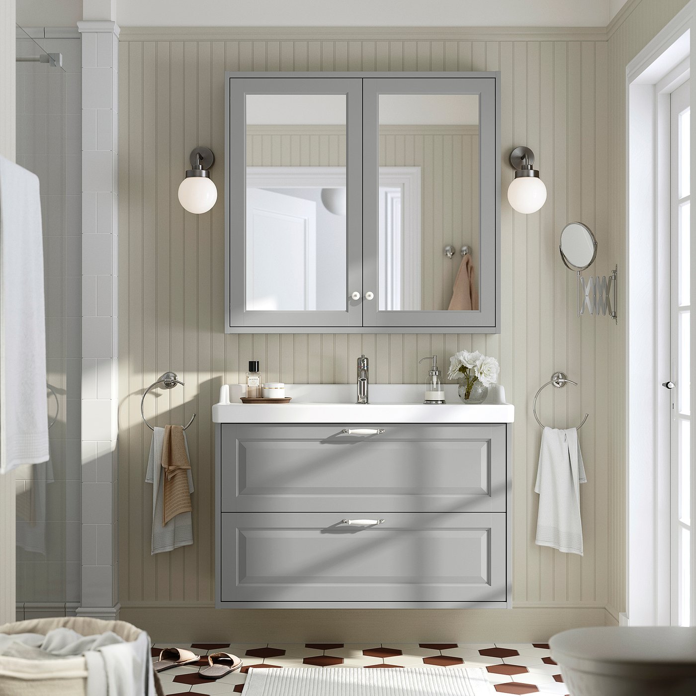 Grey bathroom cabinet with mirror, lights, & towels. Minimalist decor with light grey walls & geometric floor tiles.