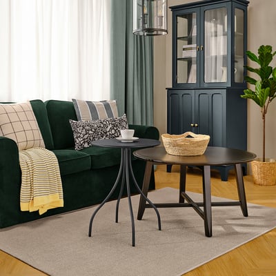 Modern living room with dark green sofa, dark anthracite TÅNEBRO side table, black accents, light grey rug, and potted plant.