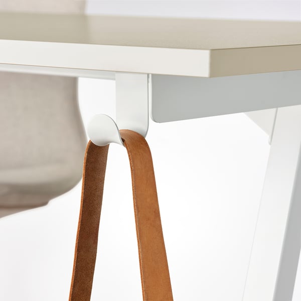 Close-up: white desk with beige top, brown leather strap hooked on side.