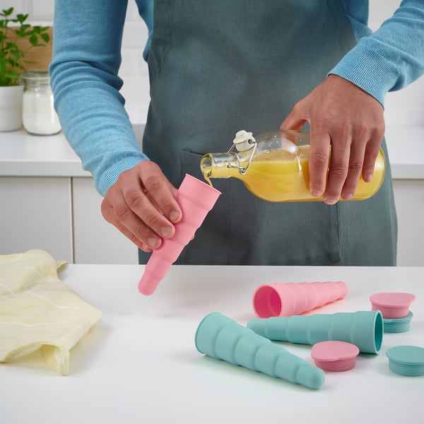 Person pours orange juice into colourful ice pop moulds on a kitchen counter, using the UPPFYLLD product.