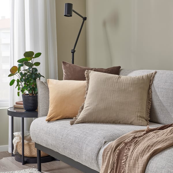 Rainbow-colored cushions on couch, plant, lamp, curtain, and basket, with VALLKRASSING pillow in foreground.