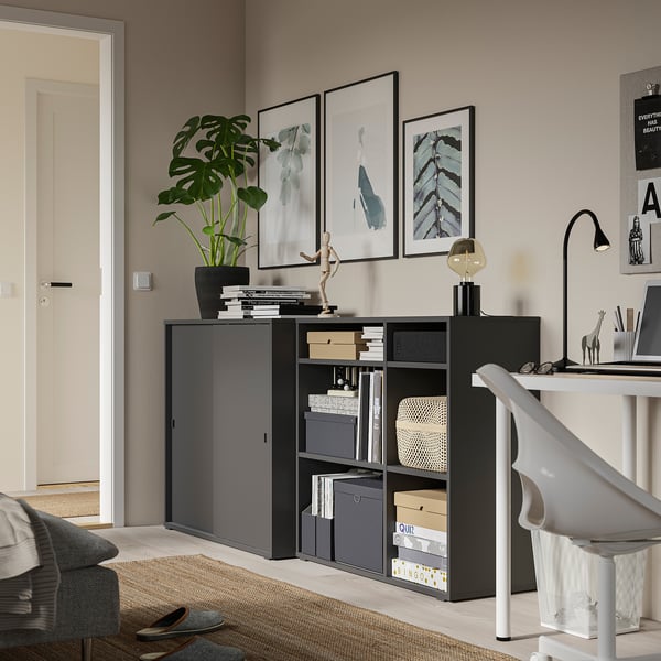 Home office with black storage unit, desk, plants, and art.