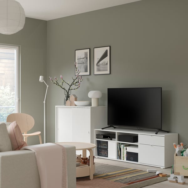Modern living room with white tv stand, beige chair, colourful rug, and green walls.