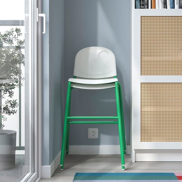 A white and green junior chair placed in a room, ideal for kids to sit at a table, with stackable and anti-slip.