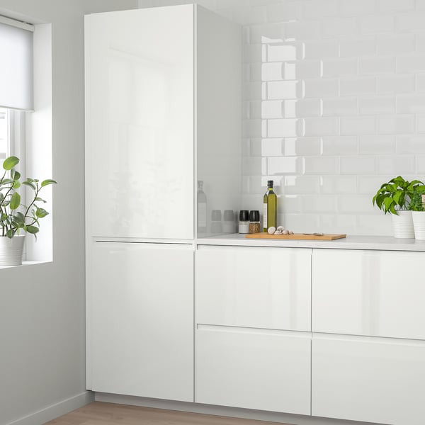 High-gloss white kitchen cabinets with integrated handles, sleek design, potted plants, clean countertop, minimalist style.