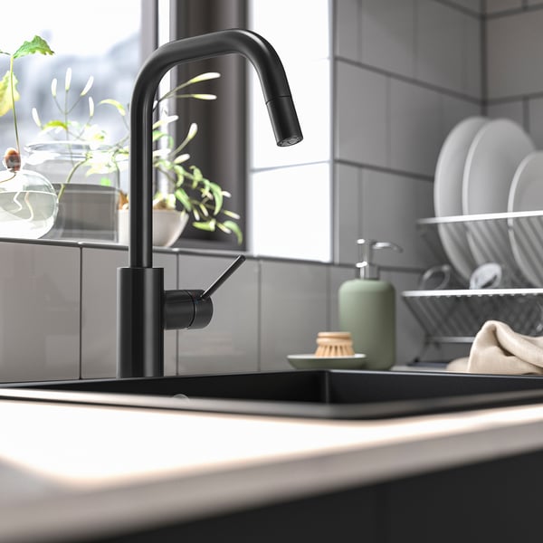 Modern kitchen sink with black pull-out tap and green soap dispenser; eco-friendly aerator.