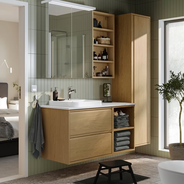 Light oak bathroom vanity with marble sink, mirror cabinet, open shelves, and hanging towels. Dark stool, tall design, modern style.
