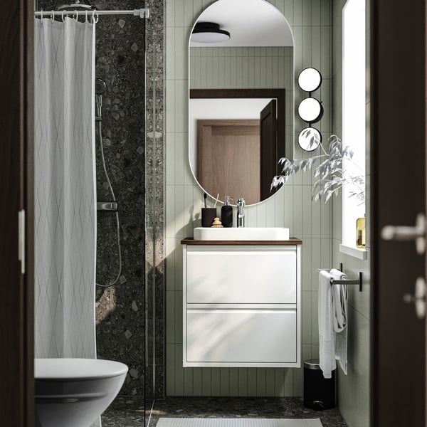 Modern bathroom with ÄNGSJÖN white wash-stand, semi-recessed basin, grey tiles, round mirror, and textured shower curtain.