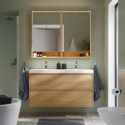 Modern bathroom with wooden cabinet, double sink, mirror, and green tiles.