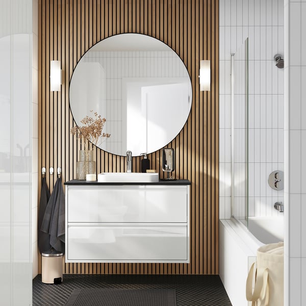 Modern bathroom with ÄNGSJÖN wash-stand, round mirror, and sleek design. Includes drawers, bathtub, and hanging towels.