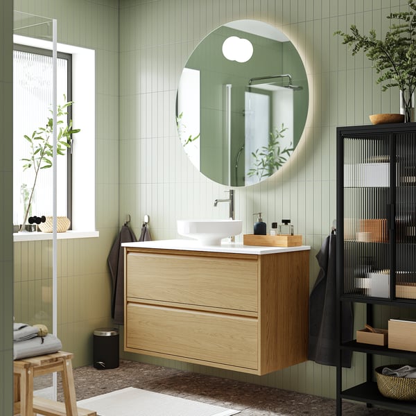 Modern bathroom: oak vanity, marble basin, green walls, natural light.
