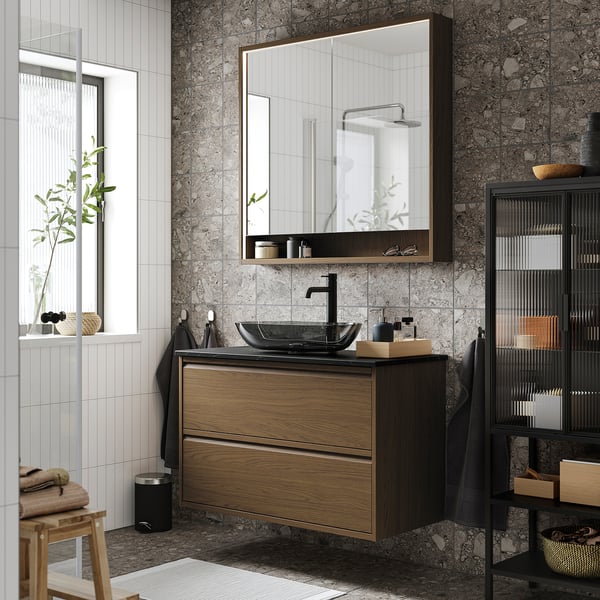 Modern bathroom with ÄNGSJÖN dark brown floating vanity, glass basin, large mirror, black shelving, and square window with white blinds.
