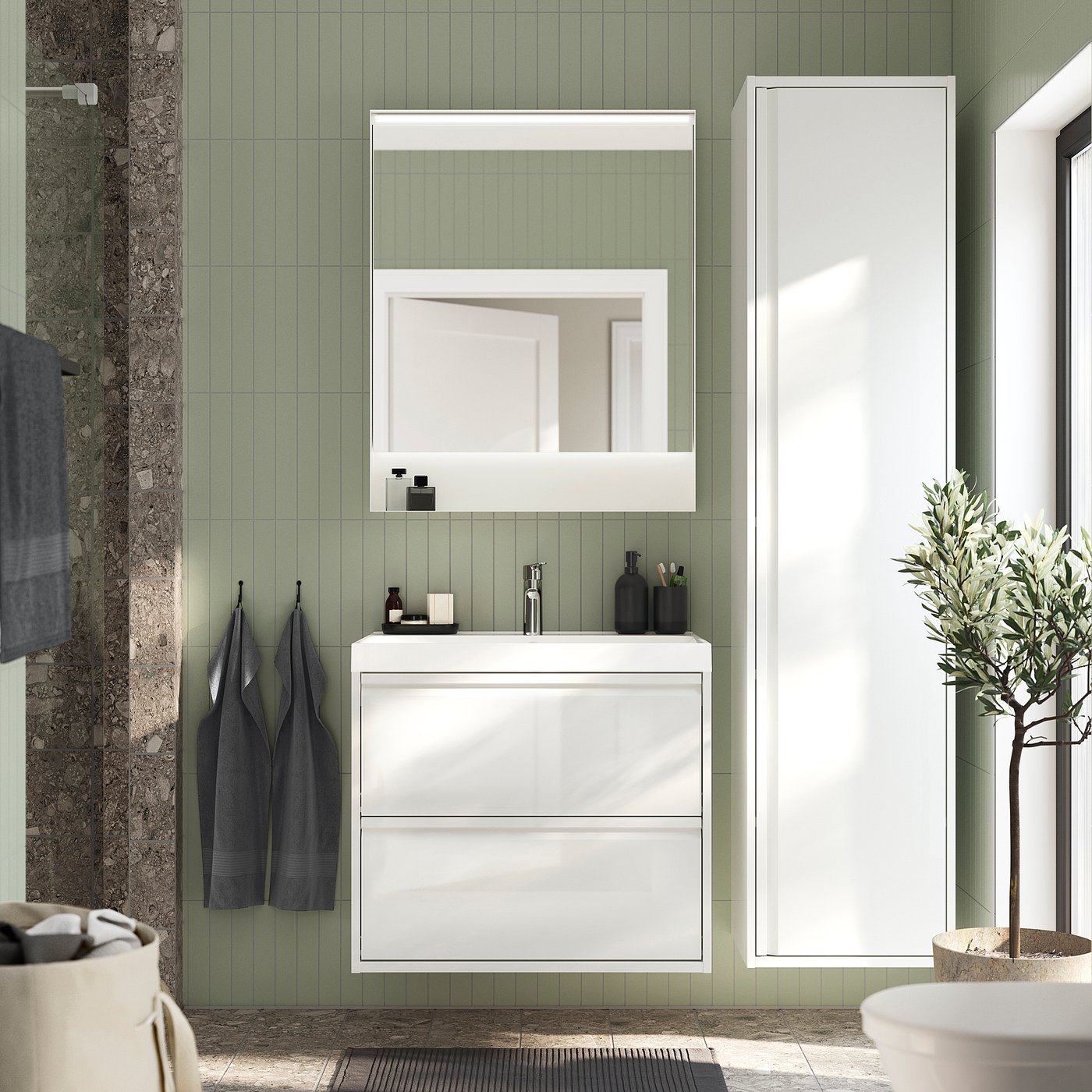 Modern bathroom vanity with sleek handles, sage tiles, dark towels & plant.