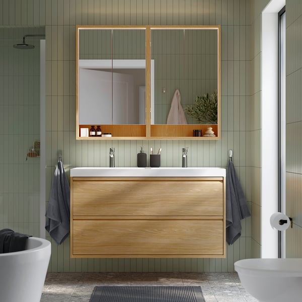 Modern bathroom with large oak cabinet, sleek white counter, and large mirror, surrounded by green tile walls.
