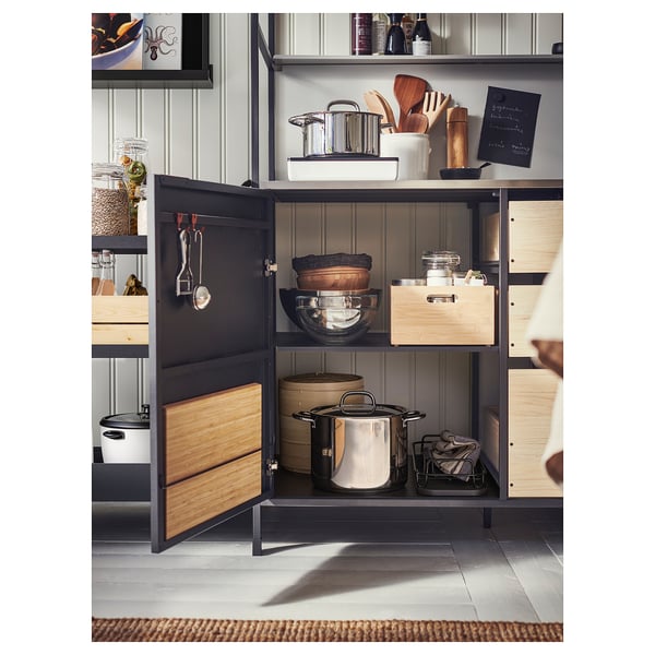 Modern kitchen cabinet with wooden doors & metal frame, storing pots, pans, & utensils neatly organised.