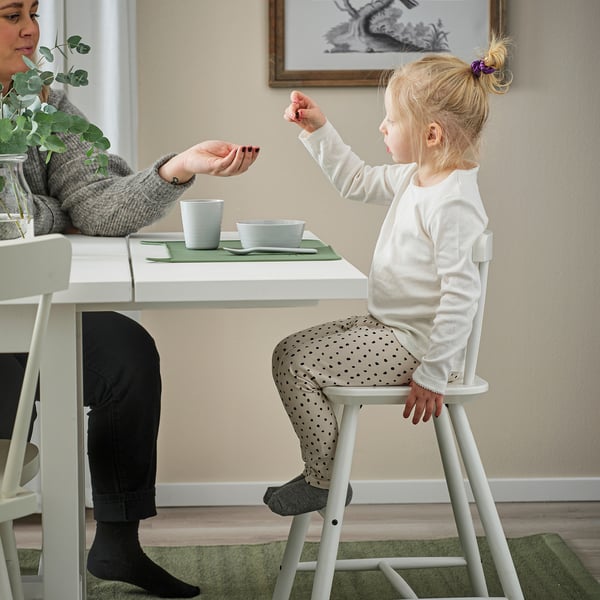 Girl hands item to person while seated on childrens chair.
